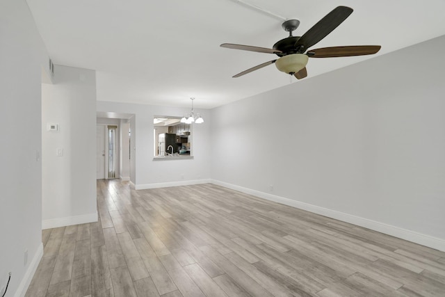 empty room featuring ceiling fan with notable chandelier and light wood-type flooring