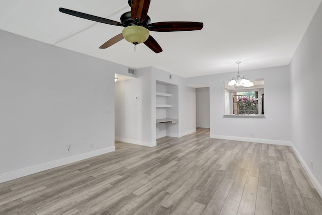 empty room featuring ceiling fan with notable chandelier, light wood-type flooring, and built in shelves