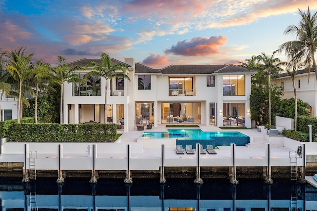 back of house featuring a balcony, a patio area, an outdoor pool, and stucco siding