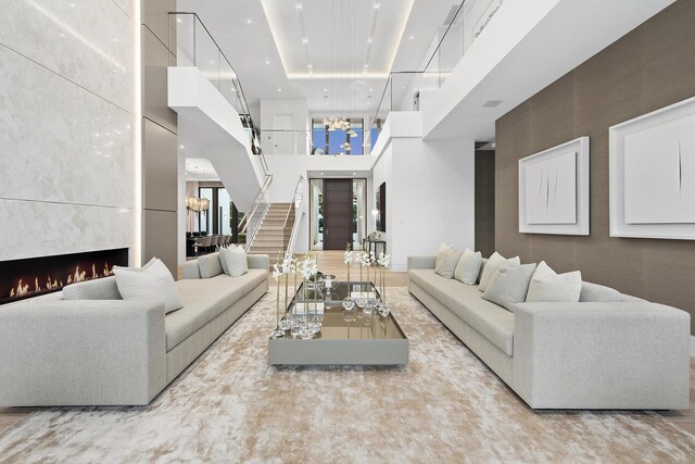 living room with light wood-type flooring, a towering ceiling, a healthy amount of sunlight, and a tiled fireplace