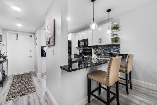 kitchen with white cabinets, light wood-type flooring, hanging light fixtures, black appliances, and dark stone countertops