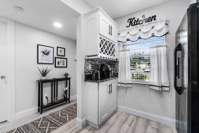 kitchen with black fridge, backsplash, light hardwood / wood-style floors, white cabinetry, and dark stone countertops