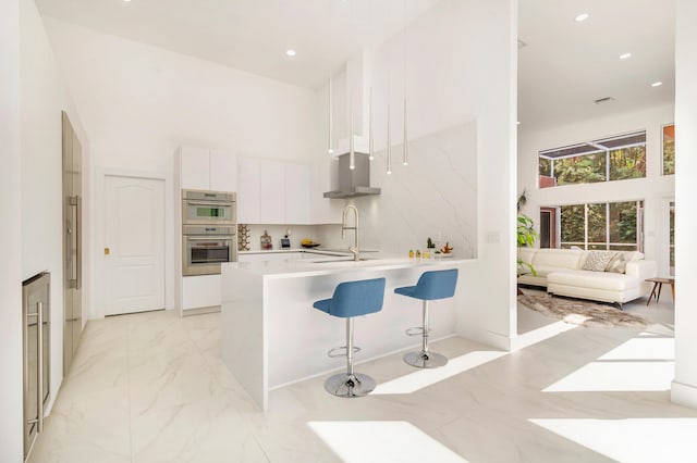 kitchen with a kitchen bar, a high ceiling, white cabinetry, hanging light fixtures, and double oven