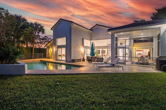 pool at dusk with ceiling fan, a lawn, an outdoor hangout area, and a patio