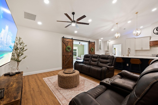 living room featuring ceiling fan with notable chandelier, lofted ceiling, light hardwood / wood-style floors, and a barn door