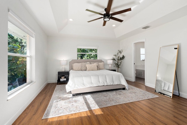 bedroom with dark hardwood / wood-style flooring, connected bathroom, ceiling fan, and a tray ceiling