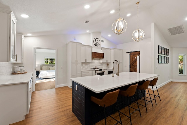 kitchen featuring a barn door, backsplash, light wood-type flooring, decorative light fixtures, and an island with sink