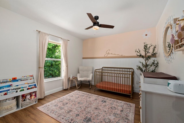 bedroom featuring hardwood / wood-style flooring, ceiling fan, and a crib