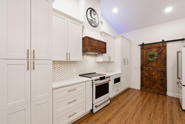 kitchen featuring a barn door, white cabinets, light hardwood / wood-style floors, white electric range oven, and tasteful backsplash