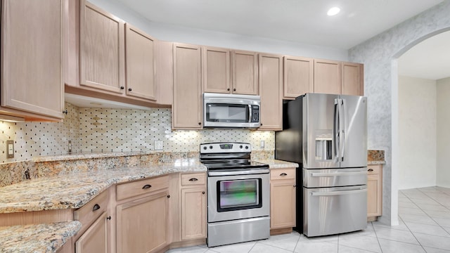 kitchen featuring light brown cabinets, light tile flooring, light stone counters, backsplash, and appliances with stainless steel finishes