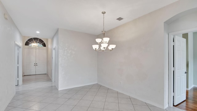 tiled spare room featuring an inviting chandelier