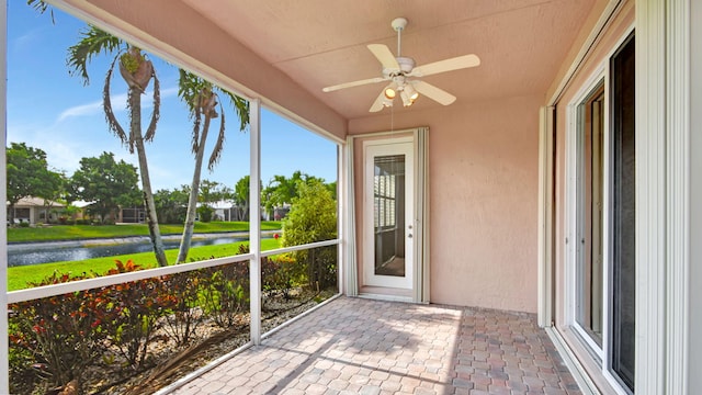 unfurnished sunroom featuring ceiling fan and a water view