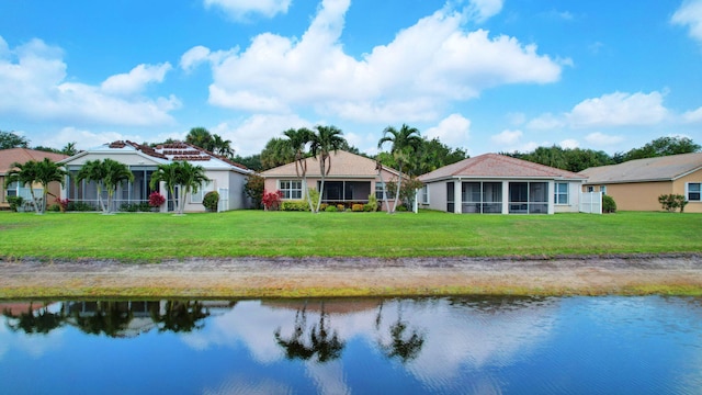 rear view of property with a sunroom, a lawn, and a water view