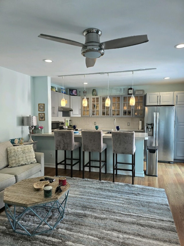 interior space featuring stainless steel refrigerator with ice dispenser, light wood-type flooring, a breakfast bar, ceiling fan, and pendant lighting