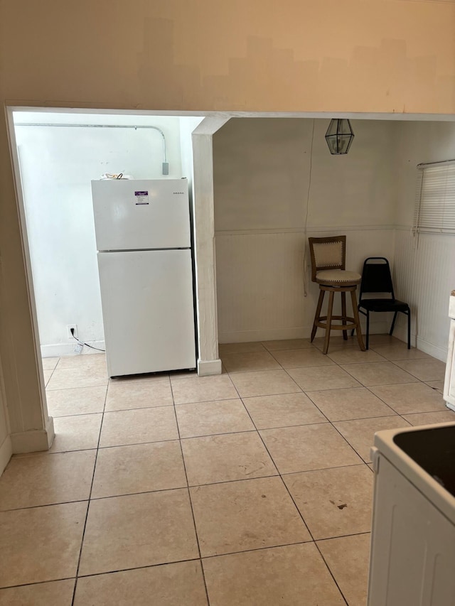 kitchen with white cabinets, a kitchen bar, light tile patterned flooring, and white fridge