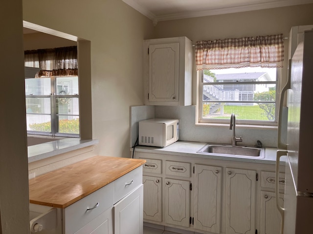 kitchen with wooden counters, ornamental molding, sink, white cabinetry, and white appliances