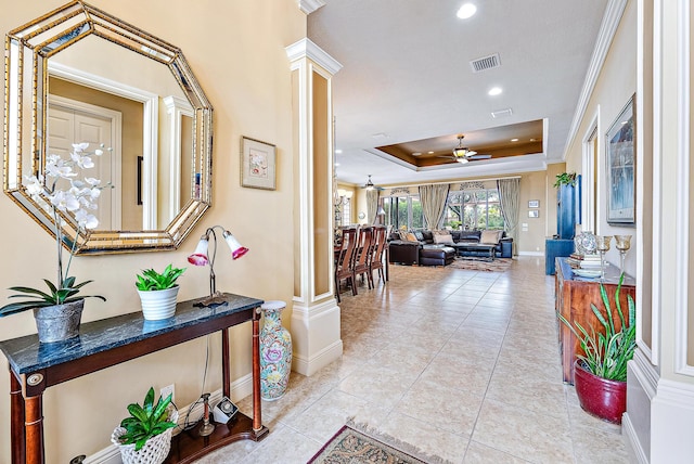 corridor featuring ornate columns, a raised ceiling, crown molding, and light tile floors