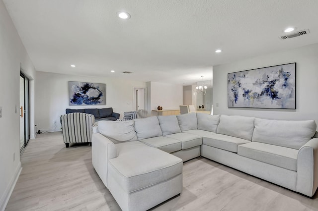 living room featuring a textured ceiling, an inviting chandelier, and light wood-type flooring