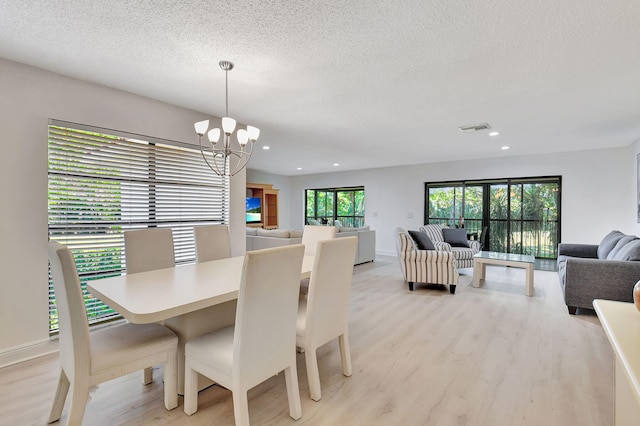 dining space with a textured ceiling, light hardwood / wood-style floors, and a chandelier