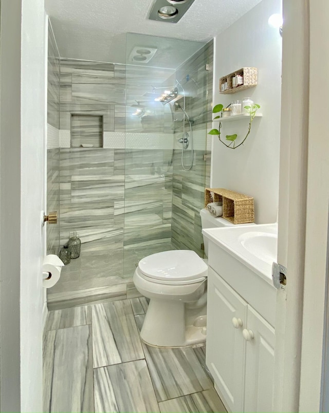 bathroom featuring toilet, a tile shower, a textured ceiling, and vanity