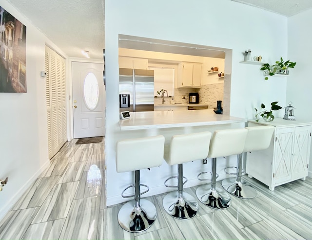 kitchen featuring tasteful backsplash, a kitchen bar, a sink, and stainless steel fridge with ice dispenser