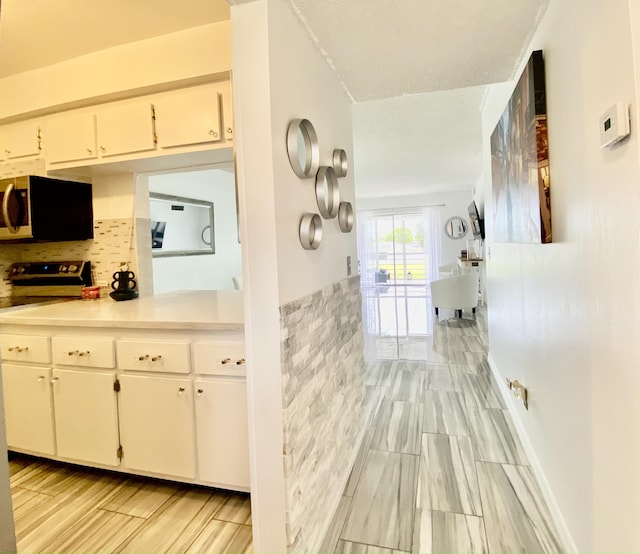 kitchen with white cabinetry, tile walls, light countertops, wainscoting, and stainless steel microwave