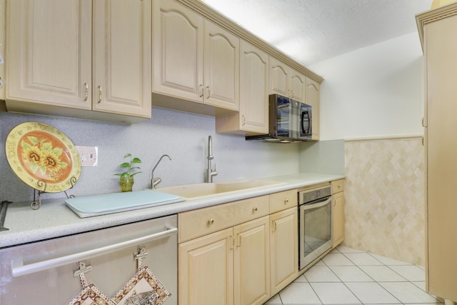 kitchen featuring a textured ceiling, light brown cabinetry, light tile patterned floors, oven, and sink