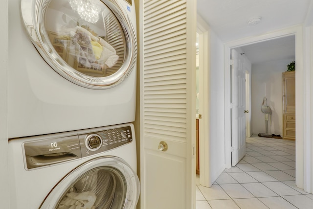 clothes washing area with light tile patterned floors, a chandelier, and stacked washer / drying machine