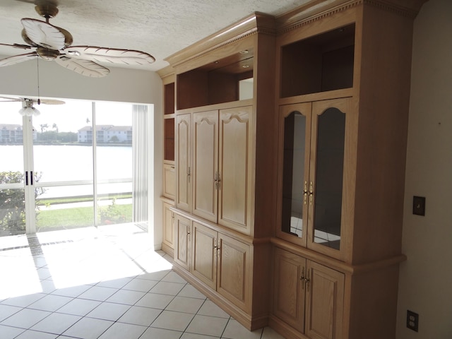 mudroom with a textured ceiling, ceiling fan, light tile patterned flooring, and a water view