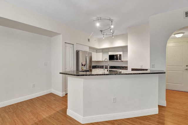 kitchen with white cabinets, light hardwood / wood-style floors, rail lighting, stainless steel appliances, and dark stone countertops