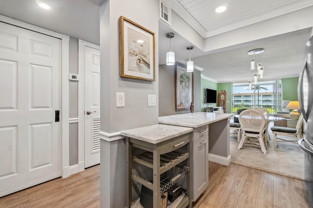 kitchen featuring hanging light fixtures, light hardwood / wood-style flooring, light stone countertops, and ornamental molding