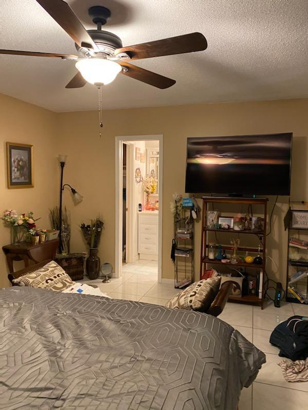 bedroom with ceiling fan, light tile floors, ensuite bathroom, and a textured ceiling