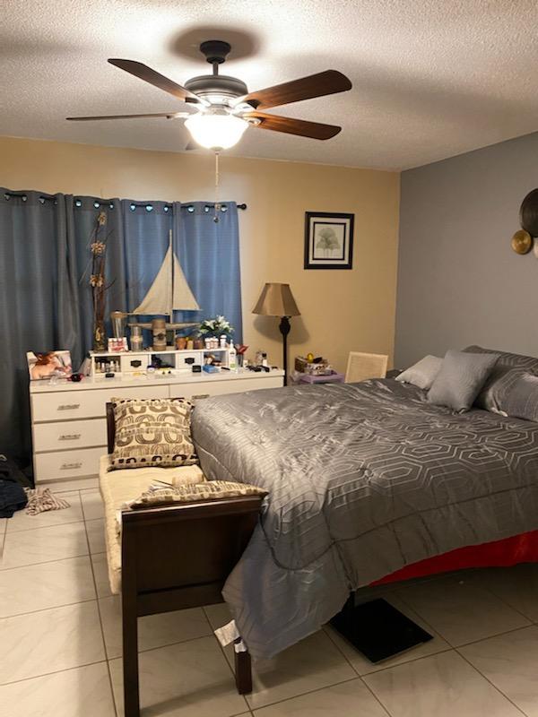 tiled bedroom with ceiling fan and a textured ceiling