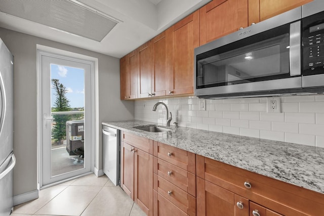 kitchen with appliances with stainless steel finishes, light stone countertops, backsplash, light tile patterned floors, and sink