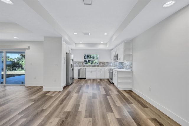 kitchen with white cabinets, a tray ceiling, backsplash, appliances with stainless steel finishes, and hardwood / wood-style flooring