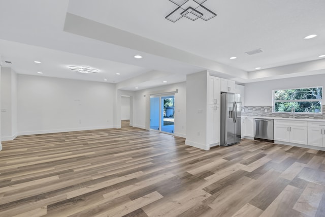 kitchen with a tray ceiling, stainless steel appliances, light hardwood / wood-style floors, and white cabinetry