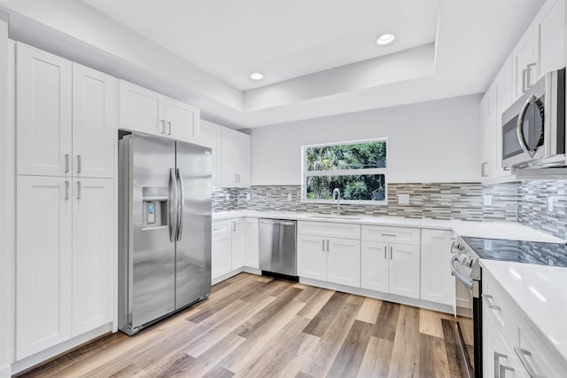 kitchen featuring white cabinets, stainless steel appliances, sink, tasteful backsplash, and light hardwood / wood-style floors