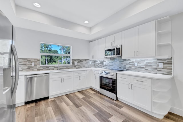 kitchen featuring white cabinets, backsplash, stainless steel appliances, sink, and light hardwood / wood-style floors