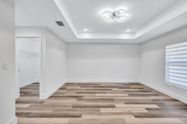 empty room with light wood-type flooring, a healthy amount of sunlight, a raised ceiling, and a textured ceiling