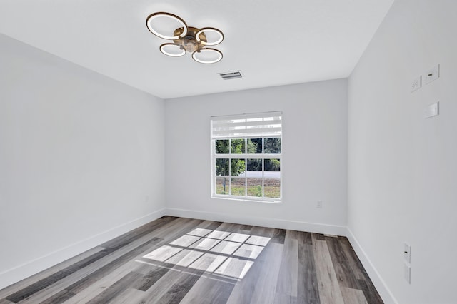 spare room featuring a chandelier and dark wood-type flooring