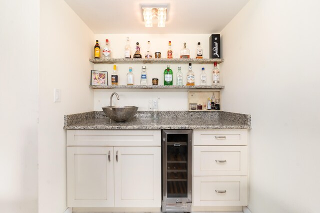 bar with light stone counters, sink, beverage cooler, and white cabinets