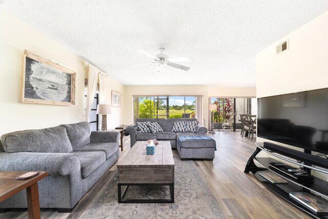 living room with a textured ceiling, ceiling fan, and dark hardwood / wood-style floors