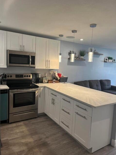 kitchen featuring appliances with stainless steel finishes, white cabinetry, dark wood-type flooring, decorative light fixtures, and kitchen peninsula