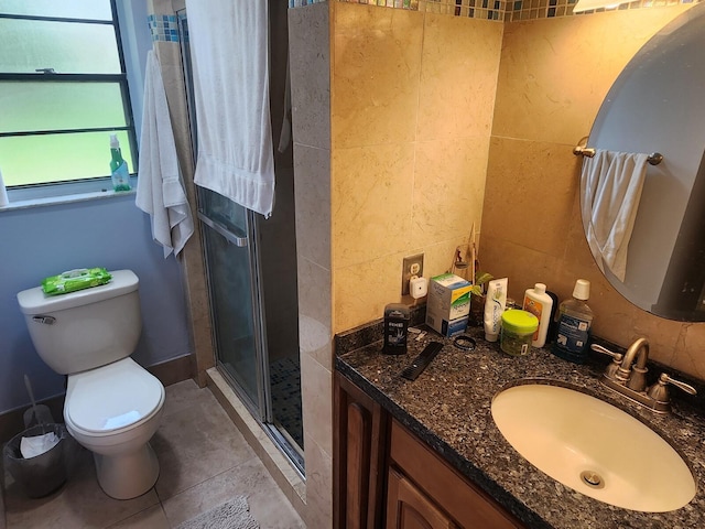 bathroom featuring tile walls, tile floors, toilet, vanity, and a shower with door