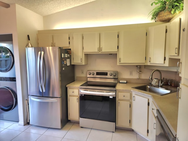 kitchen featuring sink, stacked washer and clothes dryer, stainless steel appliances, light tile patterned floors, and cream cabinets