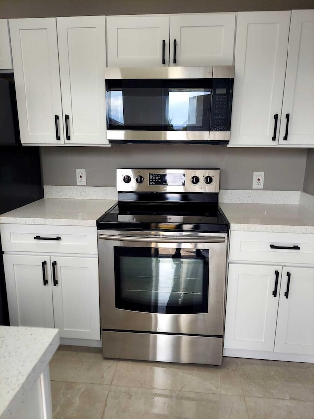 kitchen with white cabinets, light tile floors, stainless steel appliances, and light stone countertops