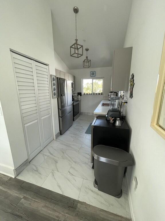 interior space featuring light tile patterned flooring, hanging light fixtures, high vaulted ceiling, appliances with stainless steel finishes, and kitchen peninsula