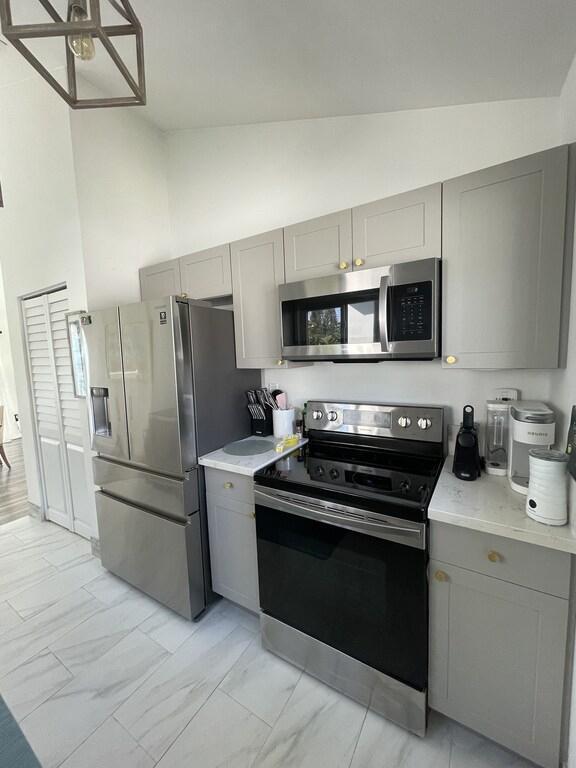 kitchen with high vaulted ceiling, appliances with stainless steel finishes, gray cabinets, and light tile patterned floors