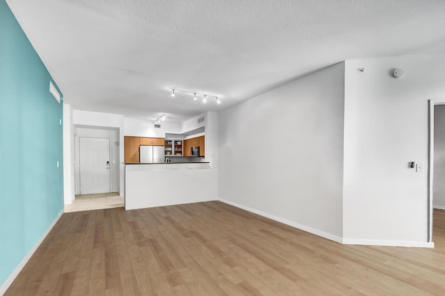 unfurnished living room featuring baseboards, a textured ceiling, and light wood finished floors