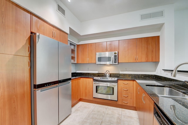 kitchen with dark stone countertops, light tile patterned floors, appliances with stainless steel finishes, and sink